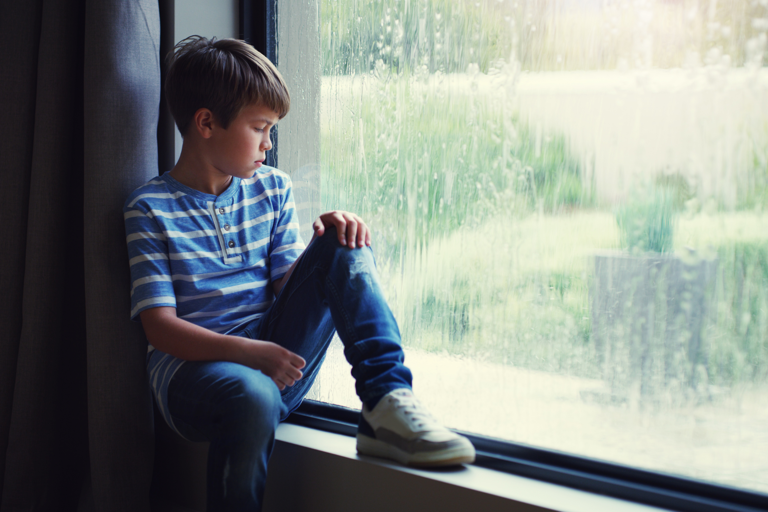 Child sitting by rainy window