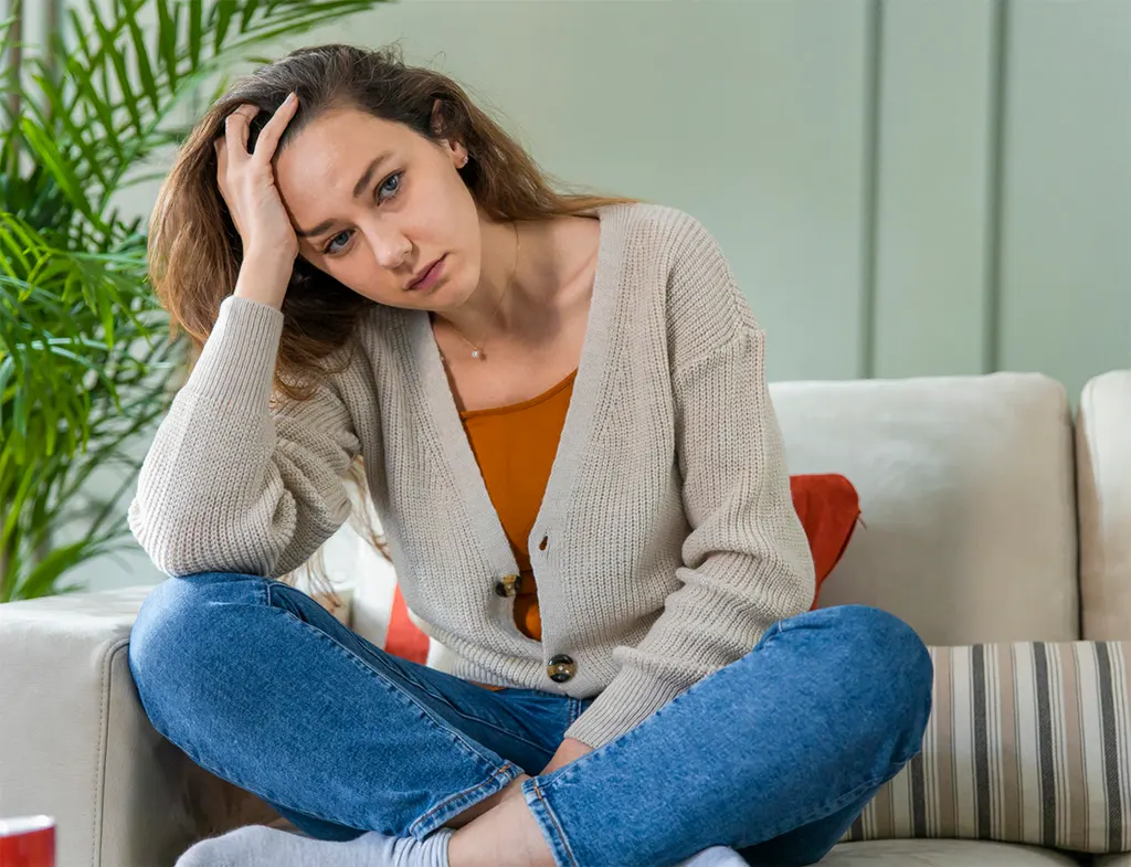 Woman sitting on a couch with her hand on her head